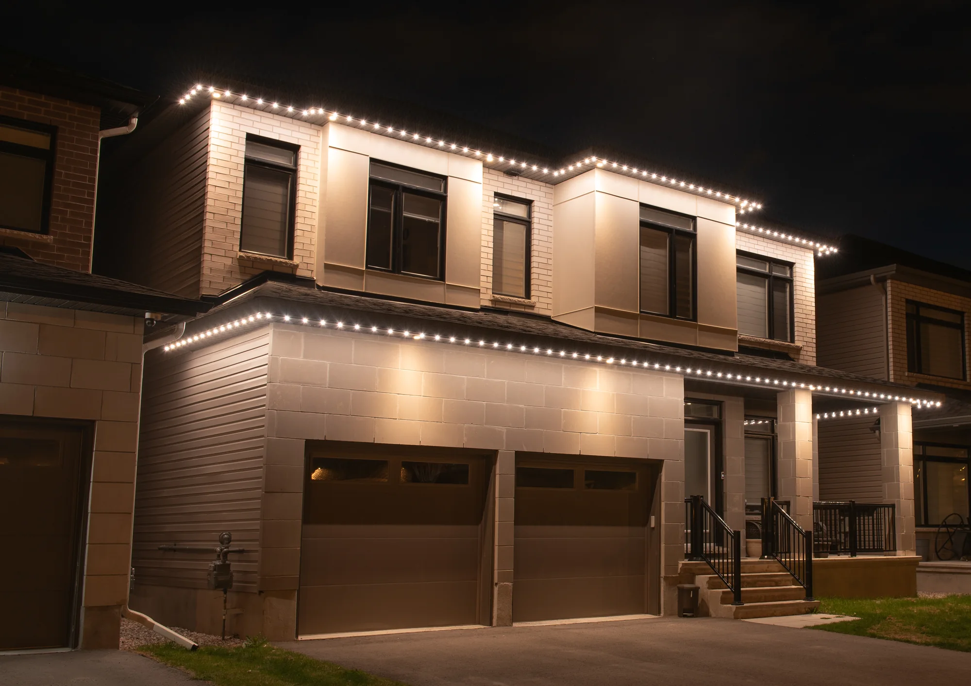A modern two story home at night with warm white lighting on both rooflines