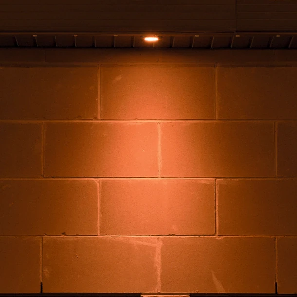 Downlight set farther from a block wall casting a broad pool of light