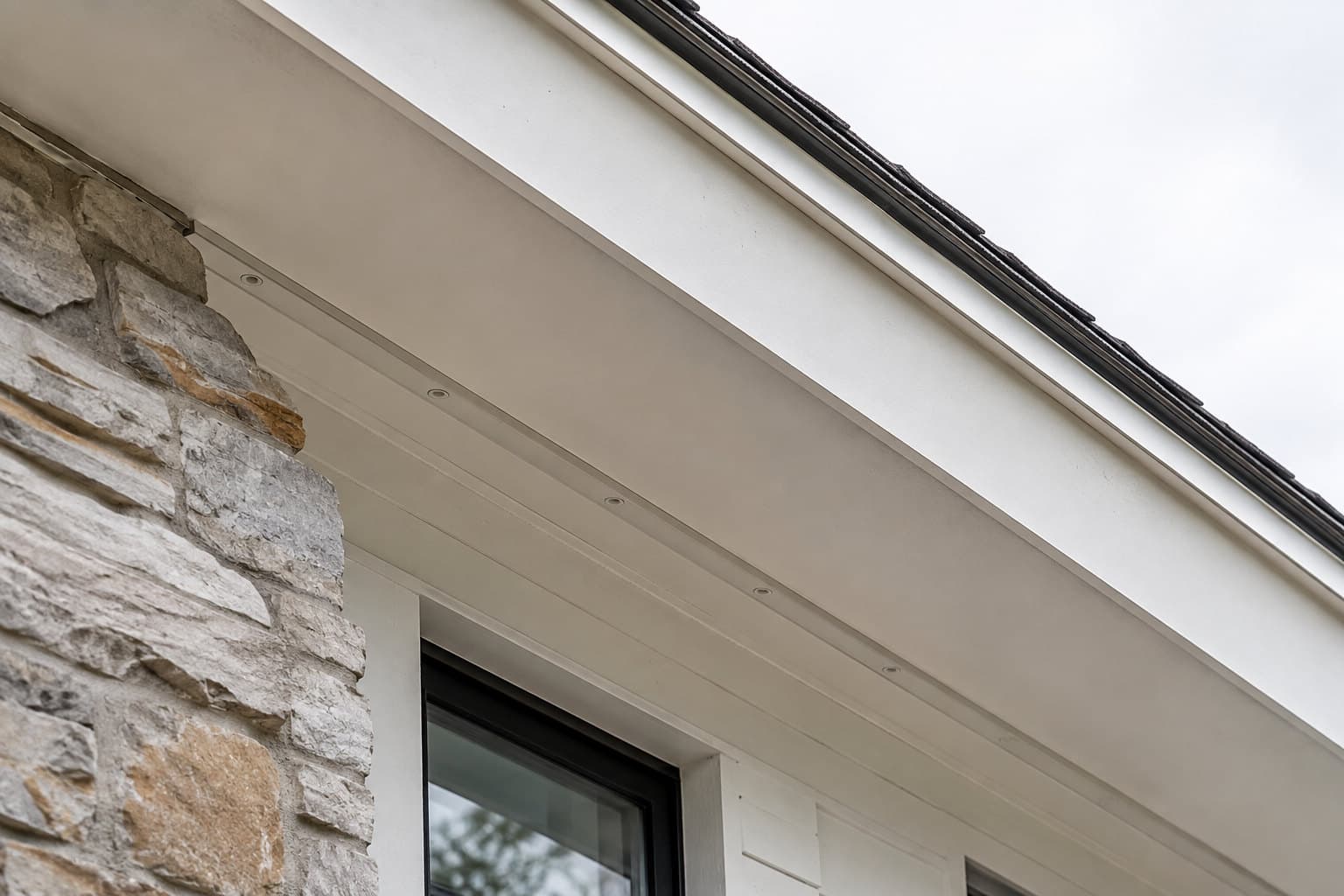 Illustration of a concealed lighting channel blended into a white soffit above a stone facade, nearly invisible in daylight